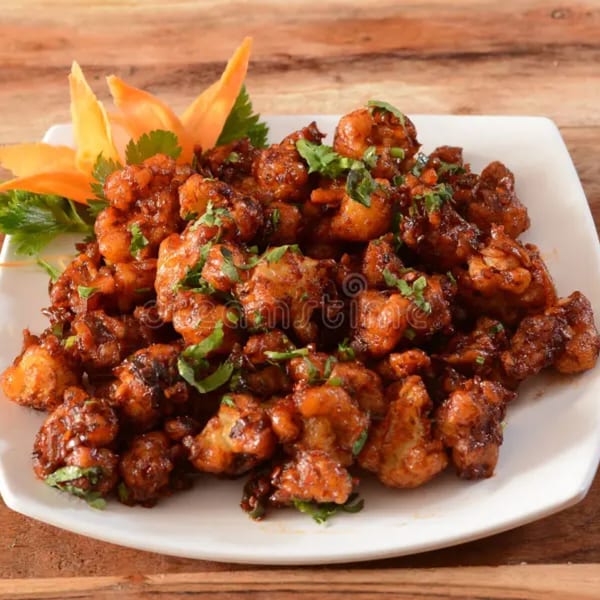 A white plate filled with Gobi Manchurian, garnished with fresh cilantro and carrot flowers, on a wooden table.
