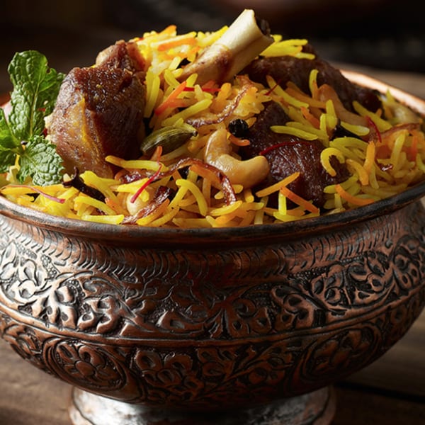 Close-up of Biryani & Bites' lamb biryani in an ornate copper bowl, garnished with mint.