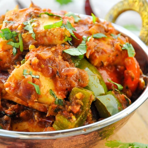 Close-up of Indian paneer curry with green bell peppers and cilantro in a copper bowl.