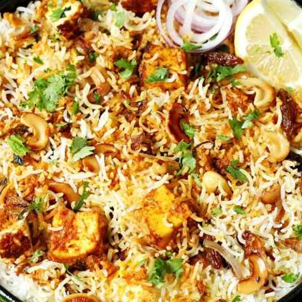 Close-up of Biryani & Bites' paneer biryani with cashews, onions, and a lemon wedge.