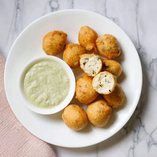 Golden-brown Indian pakoras with a creamy green dipping sauce on a white plate.