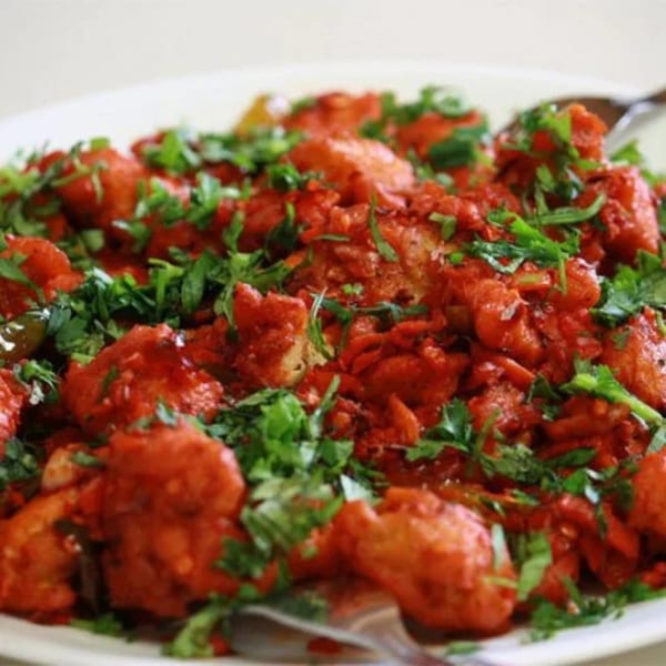 A close-up of bright red Indian chicken 65, garnished with fresh green cilantro on a white plate.