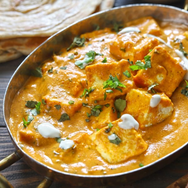 Paneer butter masala, an Indian dish, in a copper bowl with naan bread in the background.